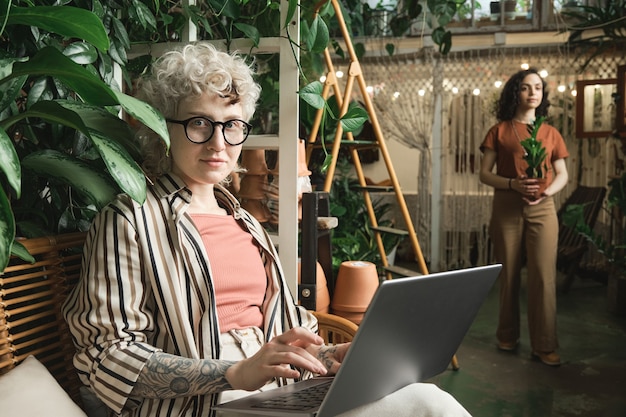 Retrato de uma jovem florista olhando para a câmera enquanto trabalhava on-line no laptop na loja de flores