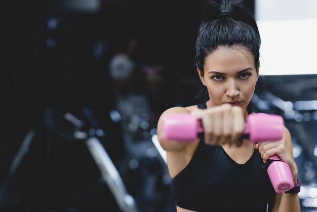 Retrato de uma jovem forte fazendo exercício com halteres Fêmea de fitness fazendo treinamento intenso no ginásio Pessoas esportivas e conceito de estilo de vida