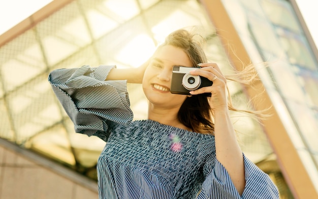 Retrato de uma jovem fotógrafa loira em um vestido com uma câmera retro ao ar livre