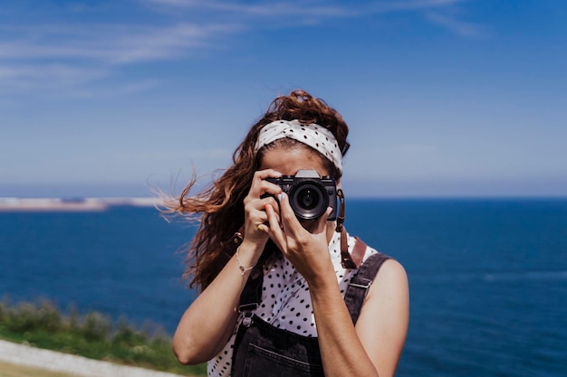 Retrato de uma jovem fotografando o mar contra o céu