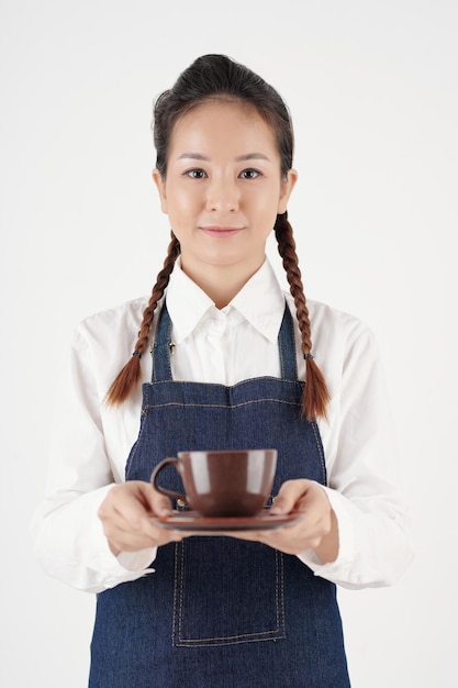 Retrato de uma jovem garçonete positiva servindo uma xícara de café saboroso ao cliente em uma cafeteria.