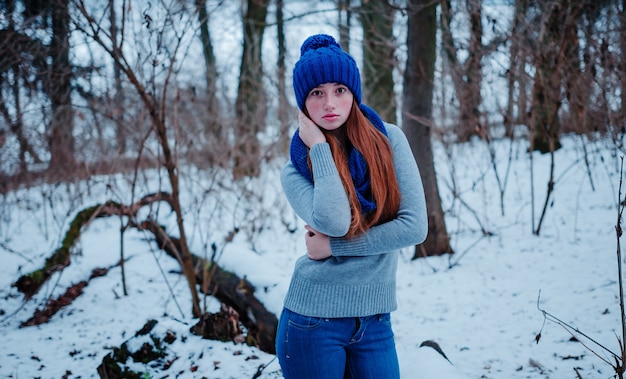 Retrato de uma jovem garota de cabelo vermelho com sardas vestindo no chapéu de malha de lã azul e lenço em dia de inverno.