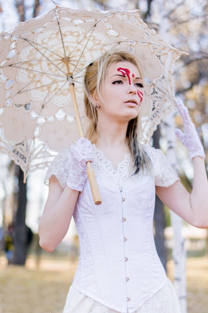 Retrato de uma jovem garota linda com sangue halloween maquiagem no rosto e vestido branco