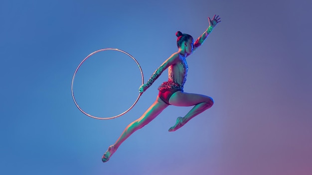 Retrato de uma jovem ginasta rítmica feminina esportiva realizando com aro isolado sobre azul