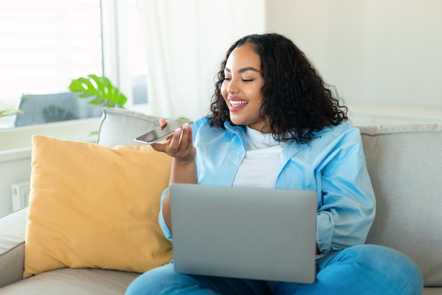 Retrato de uma jovem gordinha negra usando laptop e falando no viva-voz ditando mensagem de voz