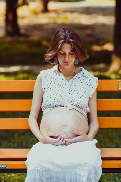 Retrato de uma jovem grávida feliz sentado num banco e olhando para a barriga com um sorriso gentil. Jovem mãe cuidando de sua barriga e olhando para sua barriga com um sorriso gentil
