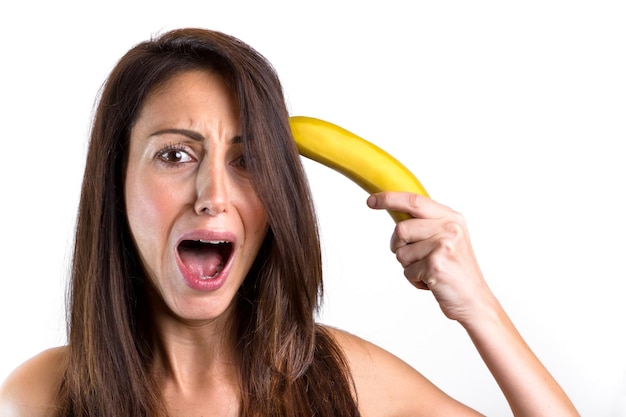 Foto retrato de uma jovem gritando enquanto segura uma banana contra um fundo branco