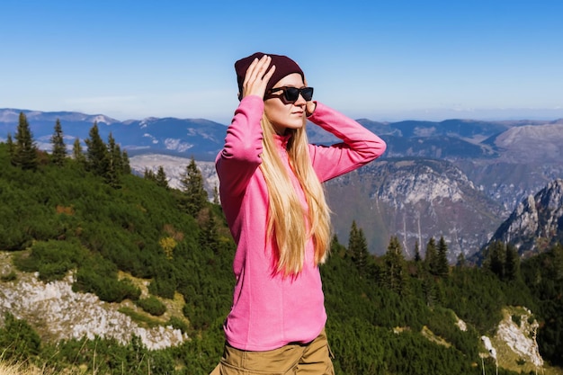 Retrato de uma jovem guia de montanha com chapéu de óculos e jaqueta rosa no fundo dos picos das montanhas em tempo ensolarado