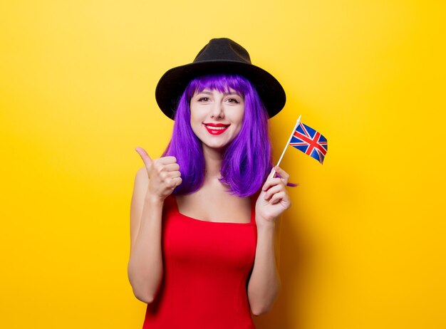 Retrato de uma jovem hipster com penteado roxo e bandeira da grã-bretanha na mão em fundo amarelo