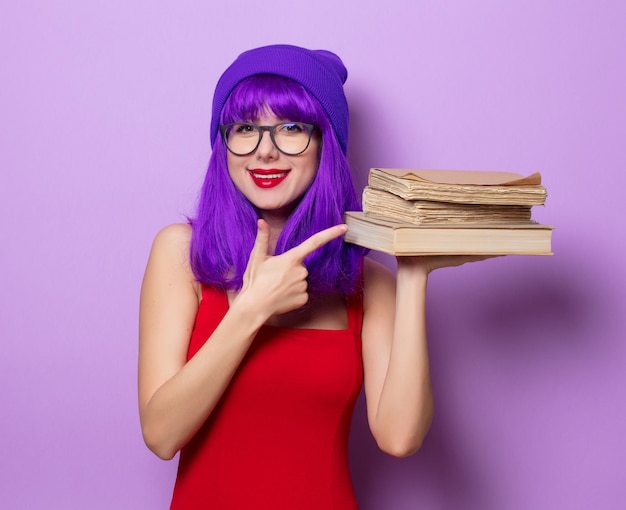 Retrato de uma jovem hipster de estilo jovem com cabelo roxo e livros sobre fundo de cor roxa