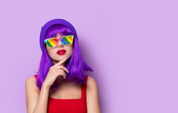 Retrato de uma jovem hipster de estilo jovem com cabelo roxo e óculos de arco-íris em fundo rosa