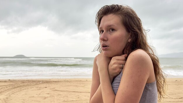 Retrato de uma jovem infeliz, deprimida, congelada, trêmula, tremendo de frio, triste mulher chateada na praia do mar, mau tempo nas férias de verão