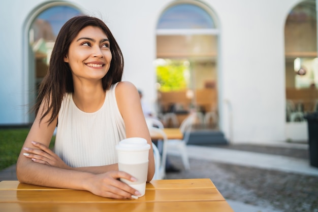 Retrato de uma jovem latina, desfrutando e bebendo uma xícara de café ao ar livre no café. Conceito de estilo de vida.