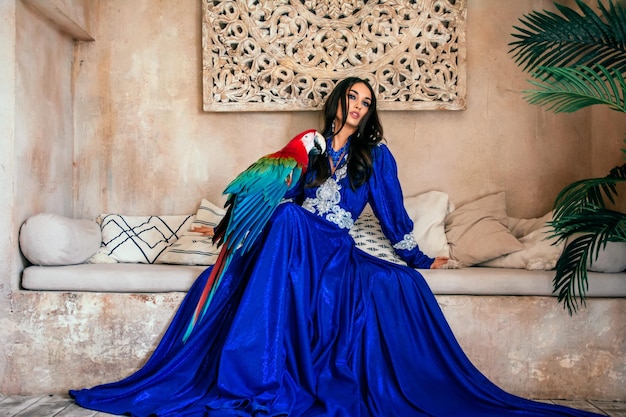 Retrato de uma jovem linda asiática em um vestido azul brilhante com um papagaio