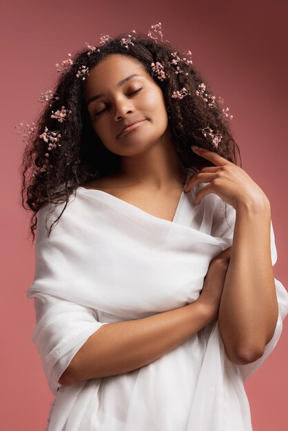 Retrato de uma jovem linda em roupão branco com pequenas flores no cabelo posando isolado sobre o fundo rosa do estúdio