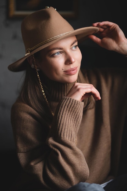 Retrato de uma jovem linda em um suéter marrom e um chapéu com aba