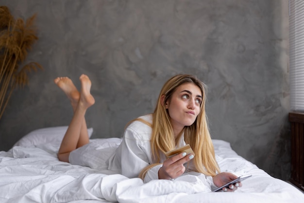 Retrato de uma jovem linda garota caucasiana deitada na cama em casa fazendo compras online