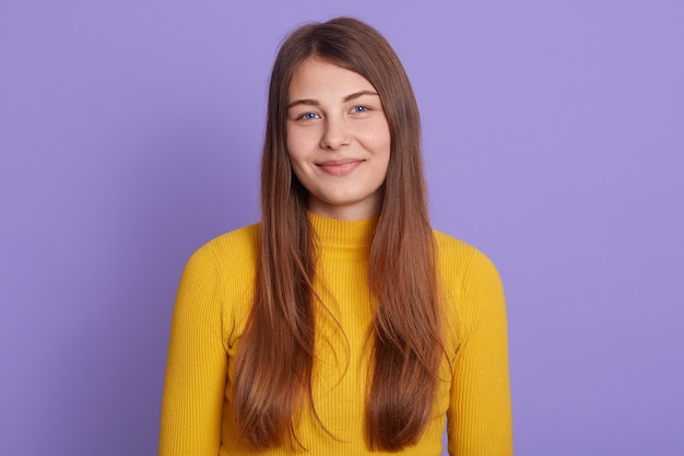 Retrato de uma jovem linda linda garota alegre, olhando para a frente com um sorriso encantador, posando isolada sobre uma parede lilás