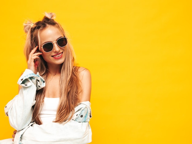 Retrato de uma jovem linda loira sorridente em roupas da moda de verão Mulher despreocupada sexy posando perto da parede amarela no estúdio Modelo positivo se divertindo dentro de casa Alegre e feliz em óculos de sol