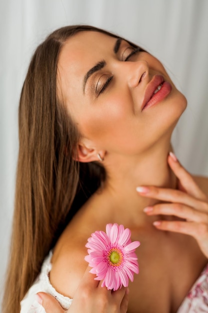 Retrato de uma jovem linda mulher de olhos castanhos de cabelos compridos com gérbera rosa sobre fundo branco Feriados da primavera Dia das mães