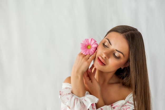 Retrato de uma jovem linda mulher de olhos castanhos de cabelos compridos com gérbera rosa sobre fundo branco Feriados da primavera Dia das mães