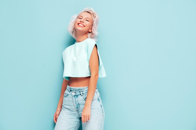 Retrato de uma jovem linda mulher sorridente em roupas da moda de verão Mulher despreocupada sexy posando perto da parede azul no estúdio Modelo loiro positivo se divertindo e enlouquecendo Alegre e feliz