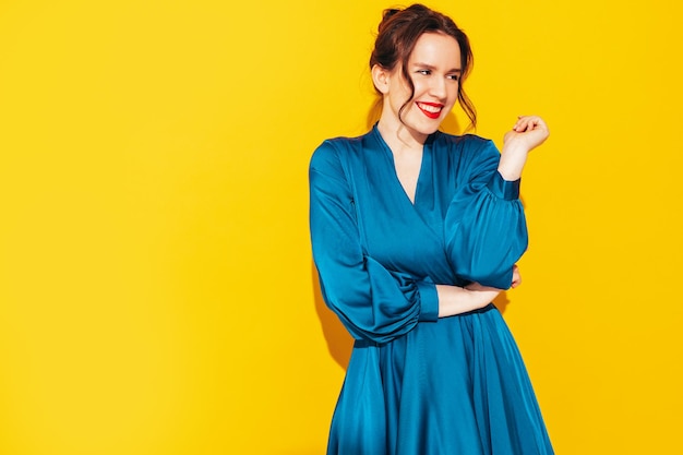 Retrato de uma jovem linda mulher sorridente no vestido azul de verão na moda Mulher despreocupada sexy posando perto da parede amarela no estúdio Modelo positivo se divertindo e enlouquecendo Alegre e feliz