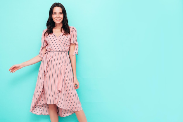 Retrato de uma jovem linda mulher sorridente no vestido rosa de verão na moda Mulher despreocupada sexy posando perto da parede azul no estúdio Modelo positivo se divertindo dentro de casa Alegre e feliz