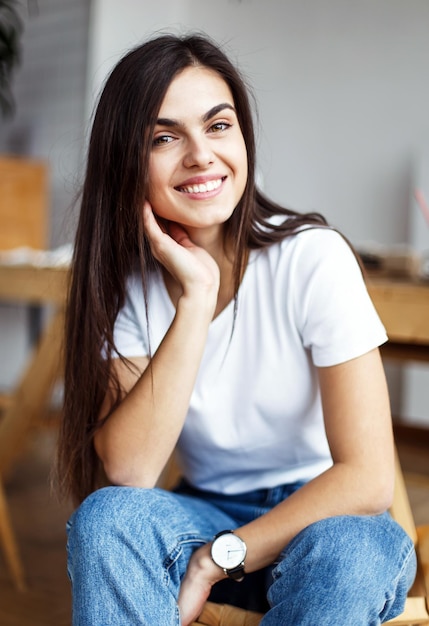 Retrato de uma jovem linda usa camiseta branca sentada na cadeira de madeira no interior