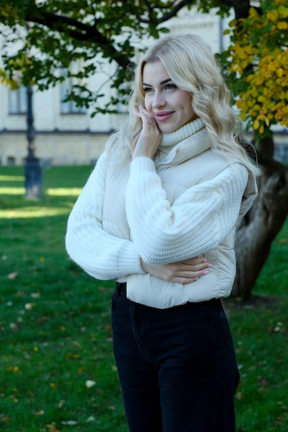 Retrato de uma jovem loira bonita com cabelos longos em um suéter branco e jaqueta em outono ensolarado em um parque da cidade