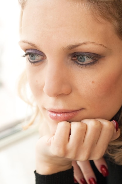 Foto retrato de uma jovem loira bonita com olhos azuis que está triste na janela