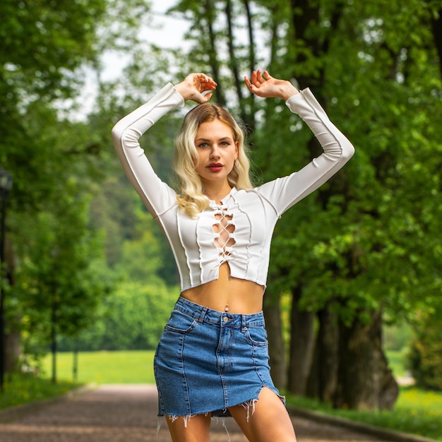 Retrato de uma jovem loira bonita em uma saia curta de ganga posando em um parque de verão