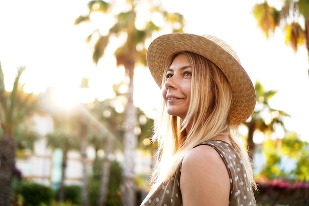 Retrato de uma jovem loira com um chapéu em um fundo tropical. luz ensolarada e cores brilhantes.