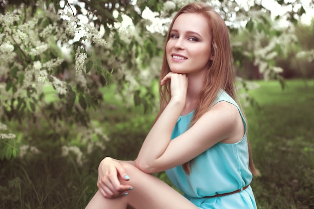 Retrato de uma jovem loira com um vestido azul. árvores em flores.