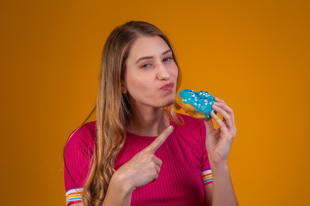 Foto retrato de uma jovem loira comendo rosquinhas coloridas deliciosas.