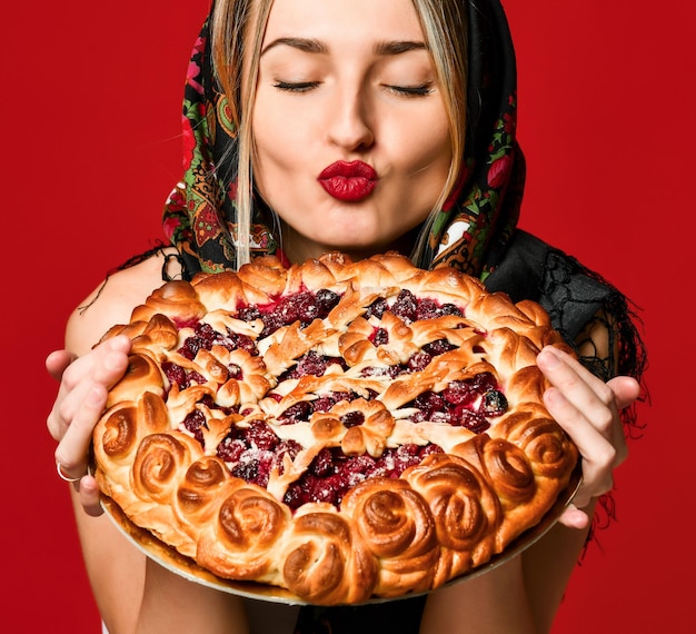 Retrato de uma jovem loira linda com lenço na cabeça segurando uma deliciosa torta de frutas caseira