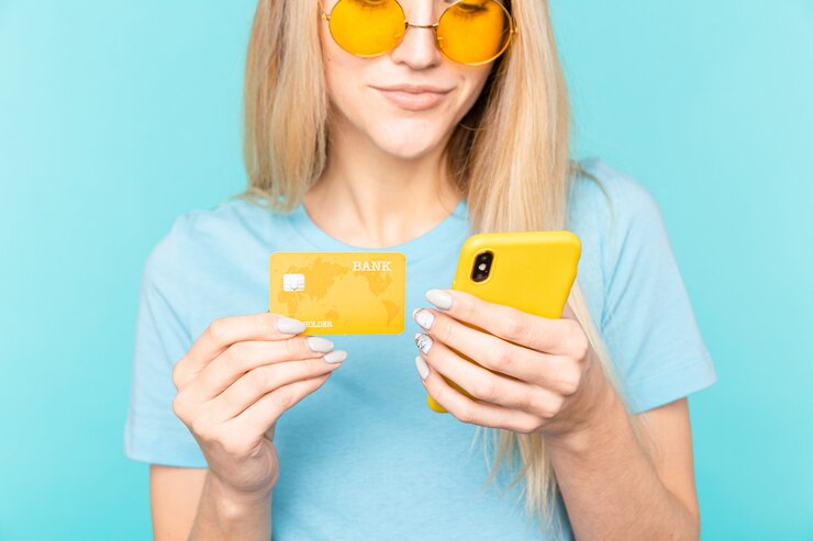 Foto retrato de uma jovem loira segurando um telefone celular e um cartão de crédito de plástico isolado em azul