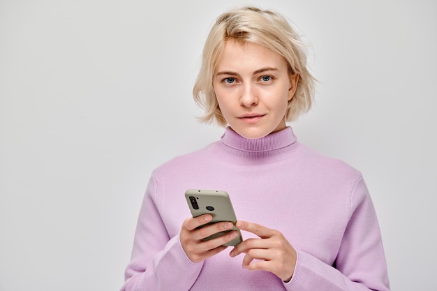 Retrato de uma jovem loira segurando um telefone móvel na mão com um rosto sorridente feliz Pessoa com smartphone isolado em fundo branco