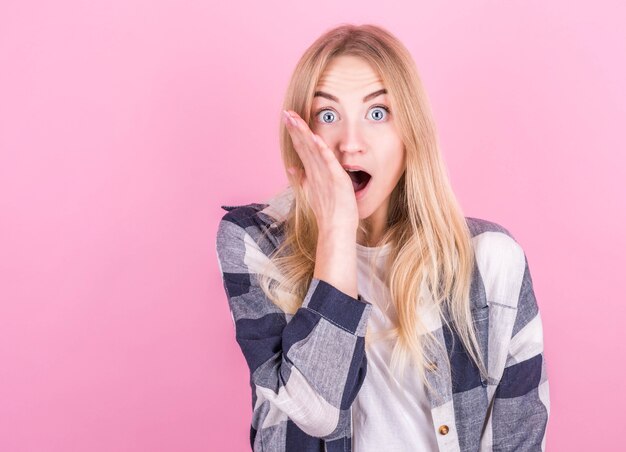 Retrato de uma jovem loira surpresa com uma camisa xadrez isolada no fundo rosa