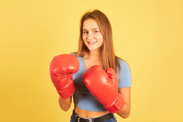 Retrato de uma jovem lutadora usando luvas de boxe vermelhas em fundo amarelo