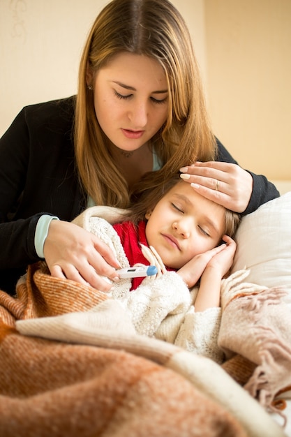 Retrato de uma jovem mãe abraçando uma menina doente na cama