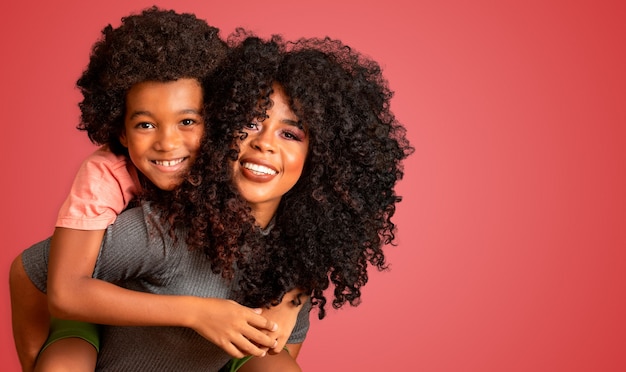 Retrato de uma jovem mãe afro-americana com o filho da criança. Fundo vermelho. Família brasileira.