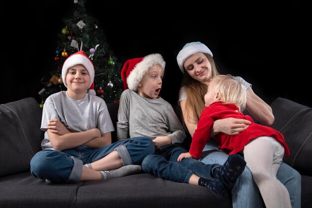 Retrato de uma jovem mãe e três filhos em casa no fundo da árvore de Natal.