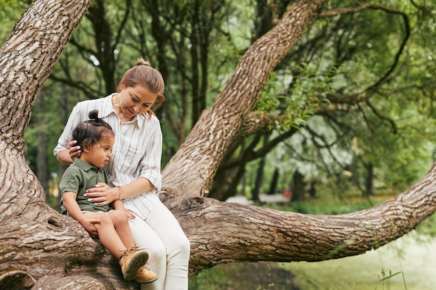 Retrato de uma jovem mãe feliz brincando com o filho no parque enquanto está sentado nos galhos de árvores, copie o espaço