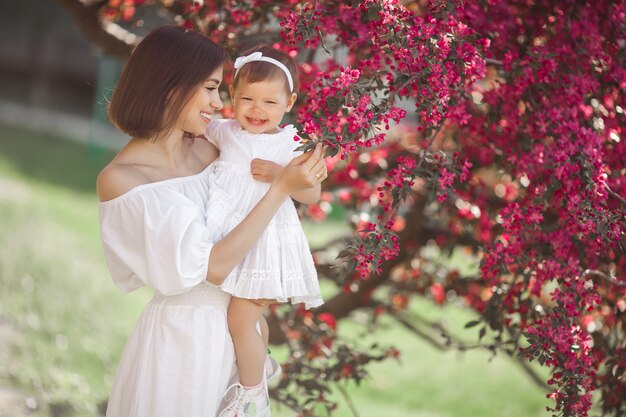 Retrato de uma jovem mãe linda com sua filhinha. Close-up ainda de amar a família. Mulher atraente, segurando seu filho em flores cor de rosa e sorrindo.