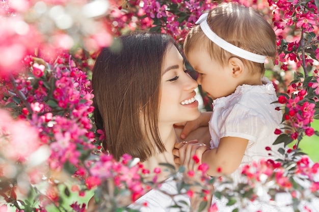 Retrato de uma jovem mãe linda com sua filhinha. Close-up ainda de amar a família. Mulher atraente, segurando seu filho em flores cor de rosa e sorrindo.