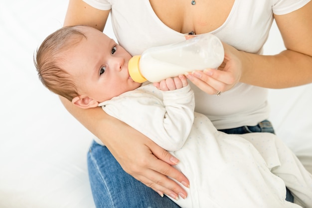 Retrato de uma jovem mãe segurando seu bebê e alimentando-o com leite em garrafa