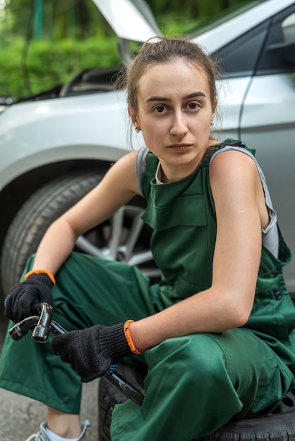 Retrato de uma jovem mecânica de uniforme perto de um carro quebrado ao ar livre