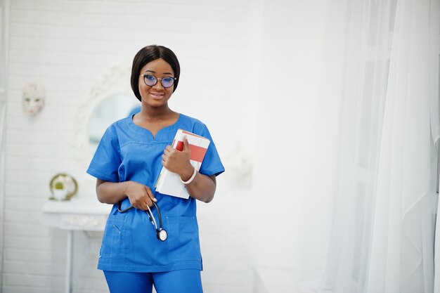 Retrato de uma jovem médica afro-americana feliz pediatra em casaco uniforme azul e estetoscópio com livros em mãos Conceito de especialista em medicina médica de saúde