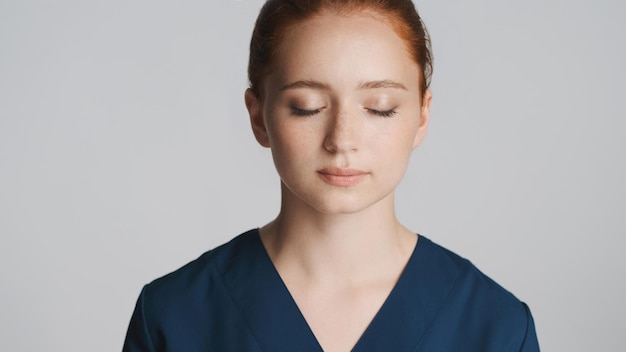 Retrato de uma jovem médica cansada sonhadoramente fechando os olhos na câmera sobre fundo branco